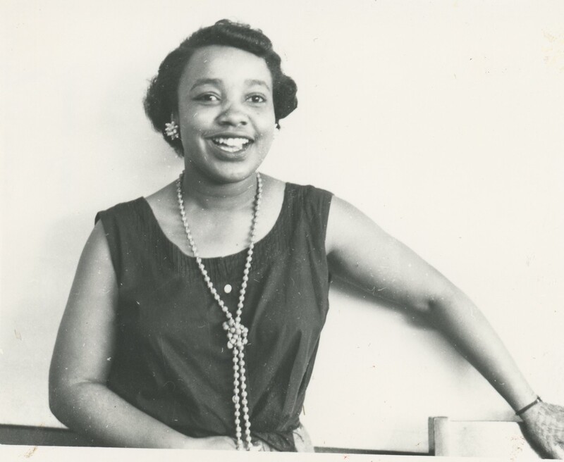 A woman smiling with a long perl neklace on.