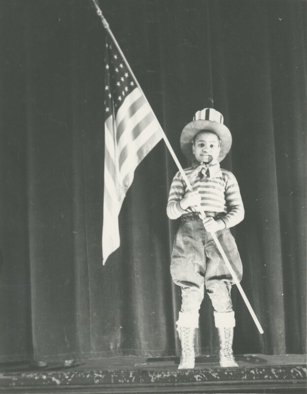 A young child holding the American flag on a stage for a program.