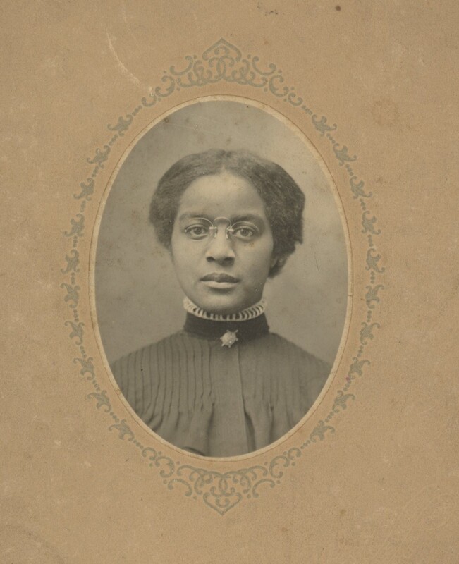 A young person wearing glasses and a tall-collard black top taking a professional portrait.