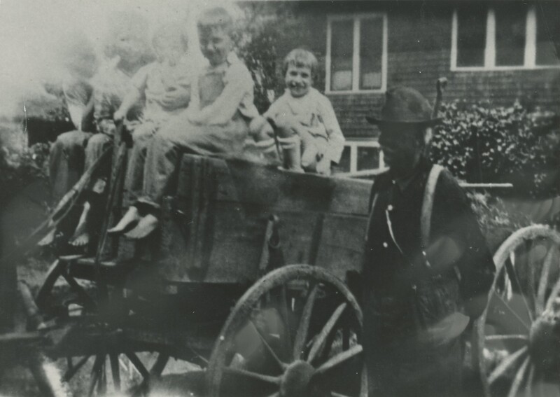 A person standing next to a horse drawn wagon with some children sat on top.