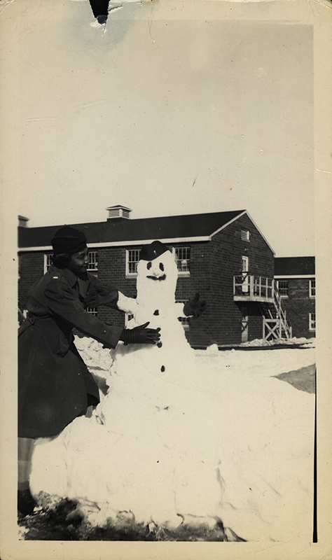 Black and white photograph of Black WAC officer building a snowman.