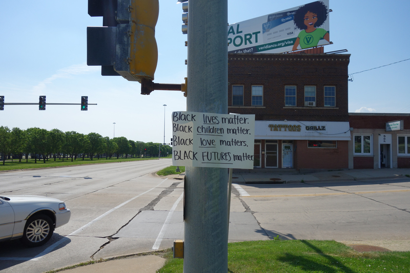 Digital image (5472 x 3648) of a white cardstock sign taped to a lightpost in Waterloo at the southwest corner of Washington and W 4th. "BLACK LIVES MATTER. BLACK CHILDREN MATTER. BLACK LOVE MATTERS. BLACK FUTURES MATTER." handwritten in black ink at anterior of sign. Red brick building with billboard in background.


Image taken on 6/4/2020 by Grout Museum District personnel. One of three such posters taped to lightposts at the intersections of Washington and W Park and Washington and W 4th in Waterloo, Iowa, before the George Floyd protest march of the night of 6/2-6/3/2020. The March began at the Black Hawk Co. Jail and was ultimately broken up by the Waterloo Police Department in Washington Park and on the 218 overpass. Grout Museum District staff collected the signs after they blew down in a storm on 6/5/2020.