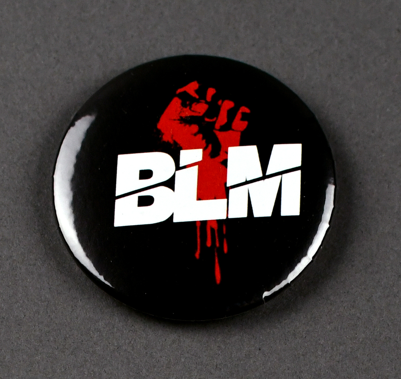 Button with safety pin clasp at posterior. Graphic at anterior printed on paper and crimped under transparent plastic covering. "BLM" in white letters over stylized red fist on black background.

Button made and sold/distributed by Amani Community Services during the 2020 George Floyd Protests in Waterloo. Amani community services is a domestic violence and sexual assault prevention agency serving African Americans in Black Hawk and Linn Counties with offices in Waterloo and Cedar Rapids.
