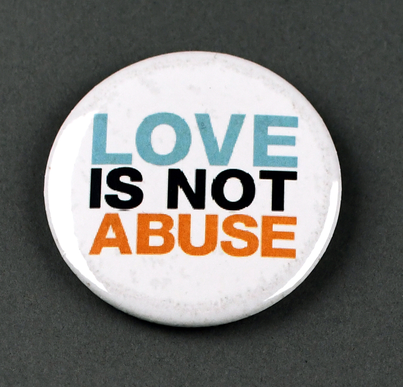 Button with safety pin clasp at posterior. Graphic at anterior printed on paper and crimped under transparent plastic covering. "LOVE IS NOT ABUSE" in blue, black, and orange on white background.

Button made and sold/distributed by Amani Community Services during the 2020 George Floyd Protests in Waterloo. Amani community services is a domestic violence and sexual assault prevention agency serving African Americans in Black Hawk and Linn Counties with offices in Waterloo and Cedar Rapids.