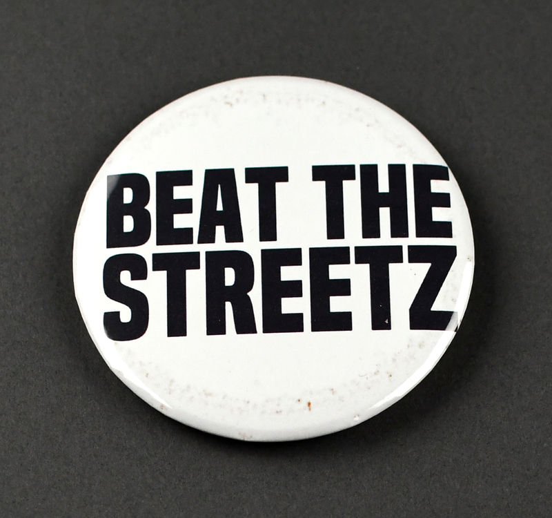 Button with safety pin clasp at posterior. Graphic at anterior printed on paper and crimped under transparent plastic covering. "BEAT THE STREETZ" in white letters on a white background.

Beat the Streetz Foundation is a Waterloo nonprofit dedicated to providing education and resources to area youth, young adults, and adults for the prevention of gun violence. It’s founder, Raynelle Walker, is sister of local citizen Greg Walker, murdered 5/19/2018. The case remains unsolved. His nickname, “Streetz,” is the origin of the Foundation’s name.  
Beat the Streetz contributed to the organization of several Waterloo protests in 2020.