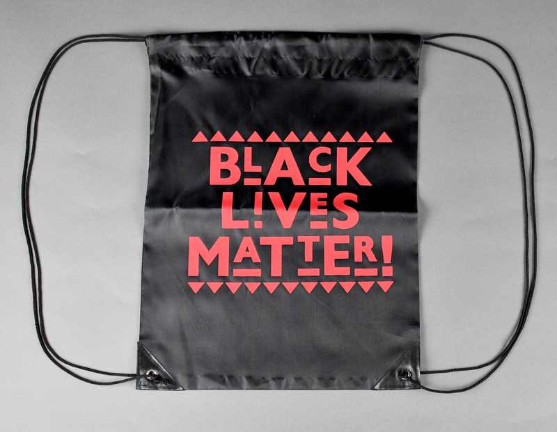 Drawstring backpack of black nylon. Machine-stitched. Nylon cord makes shoulder straps and cinch closure. “BLACK LIVES MATTER!” printed in red at center anterior. 
  
Printed and sold by Waterloo rapper Too Klean during the 2020 George Floyd Protests.
