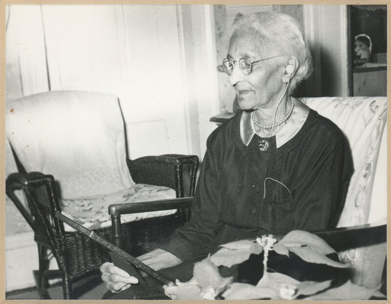 An older person sat in a home holding and looking at a framed photograph.