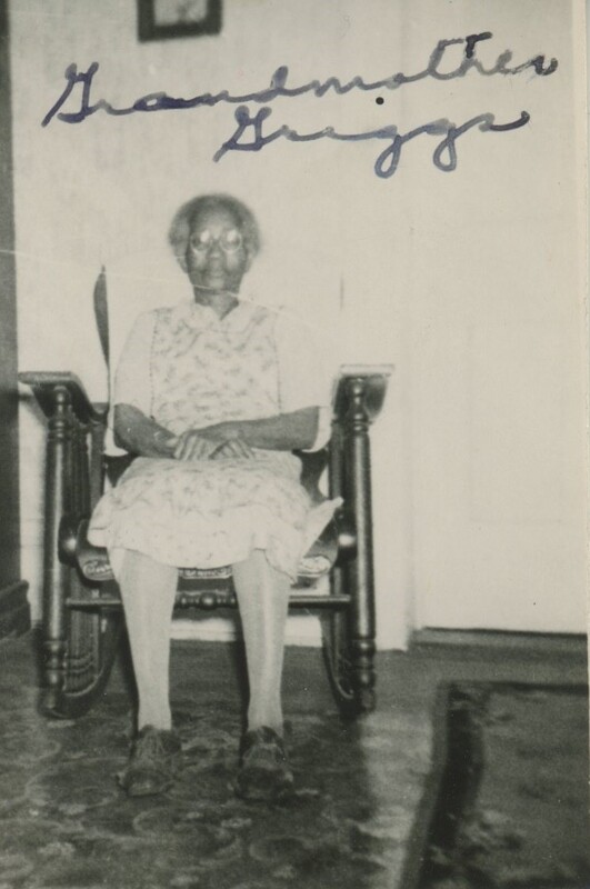 An older person sat in a rocking chair with her hads folded in her lap.