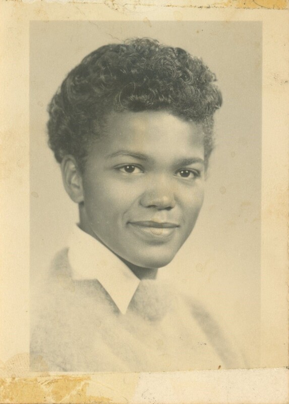 A young person looking over their shoulder and smiling for a portrait being taken from the shoulders up.
