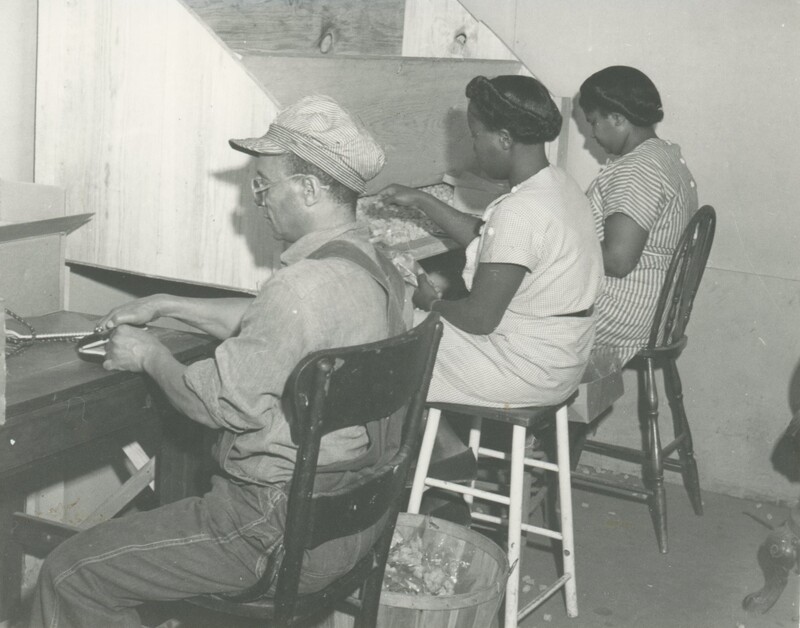 Three people are sat at work benches working with their hands.