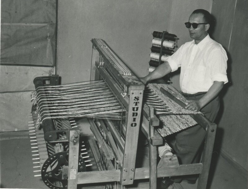A person wearing dark glasses stood behind a large looming machine.