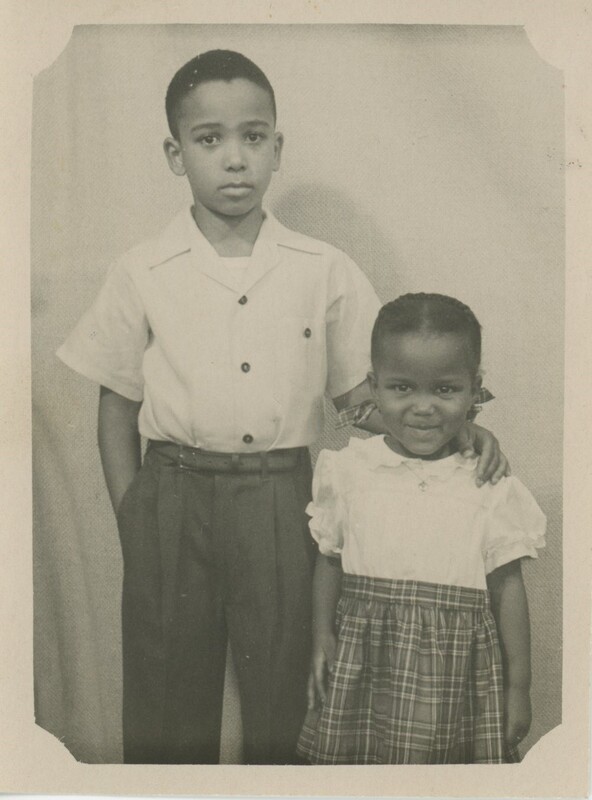 Two young children are stood next to each other. One their arm around the other childs shoulders.