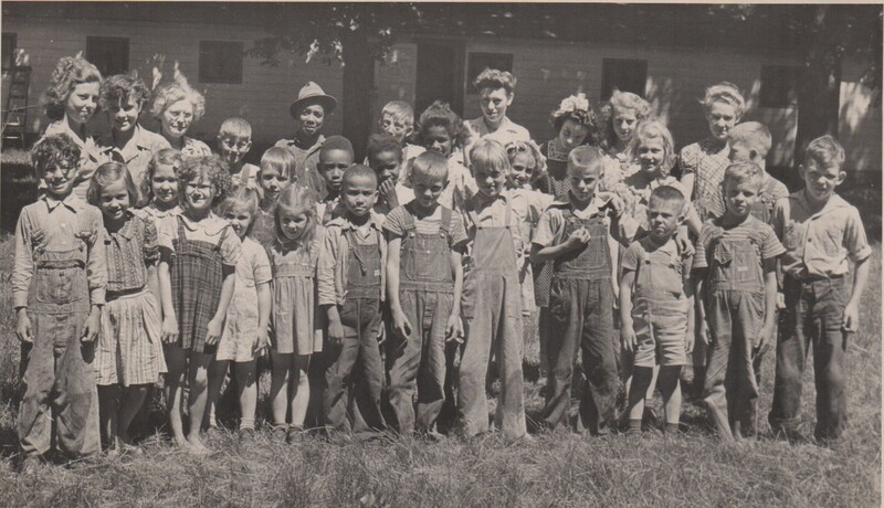 A group of children Standing next o eachother for a photo outside in the grass wth a building behind them.