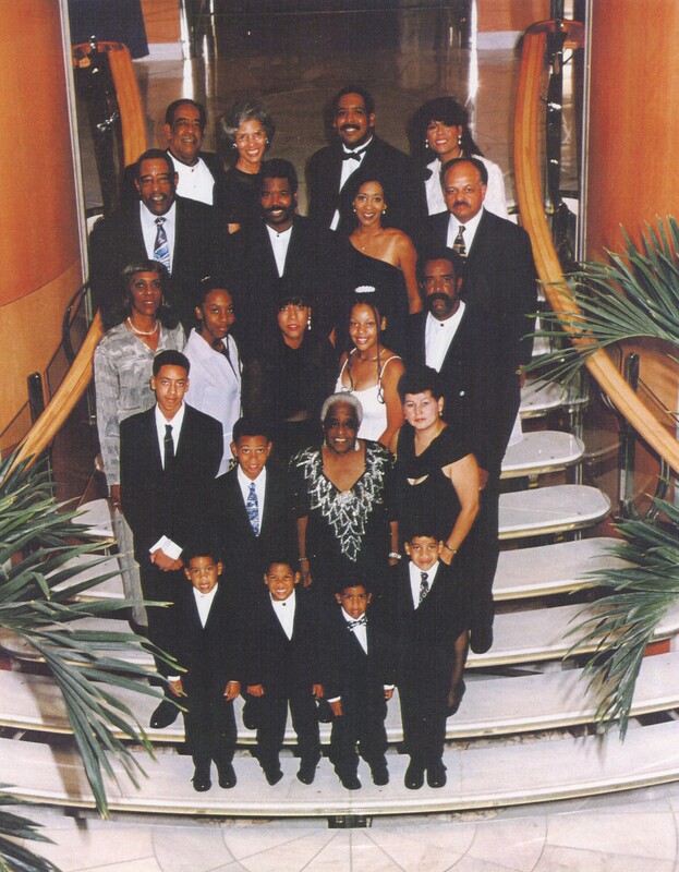 A large family are stood next to each other on a staircase taking a family photo from slightly above while on vacation.