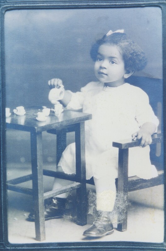 A little girl sat at a small wooden table playing with a toy tea set.