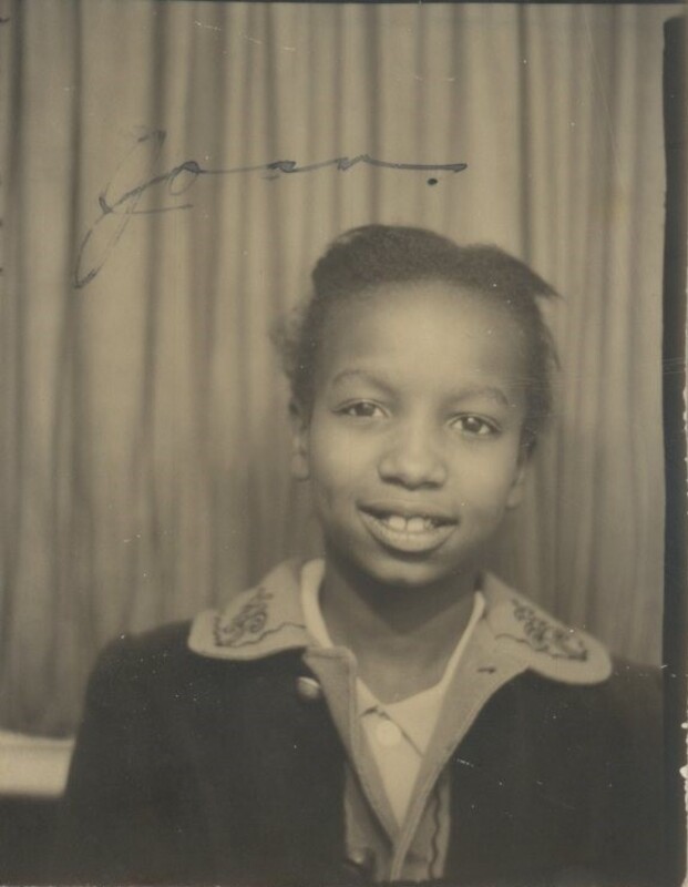 A young child smiling infront of a curtain.