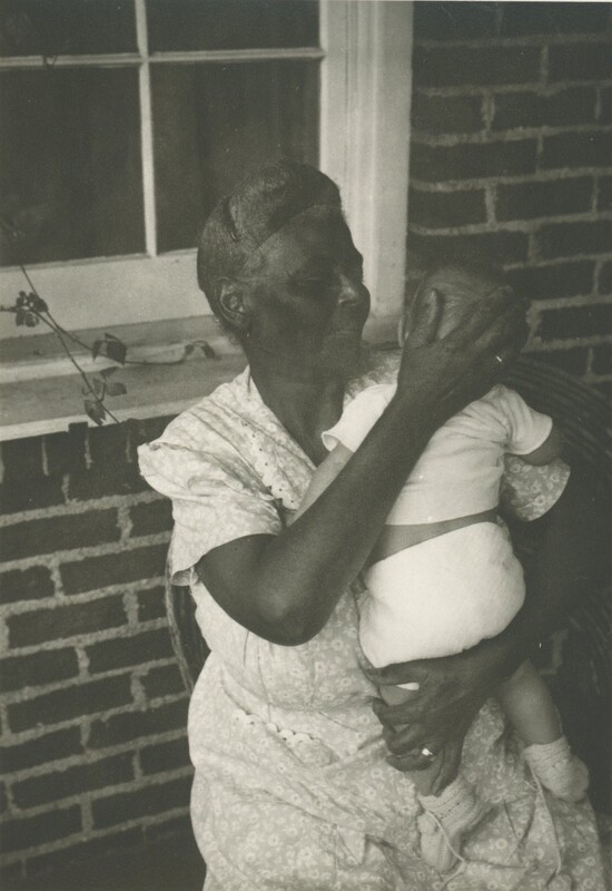 A person sat in a chair holding a baby at her should as if to burp the baby.
