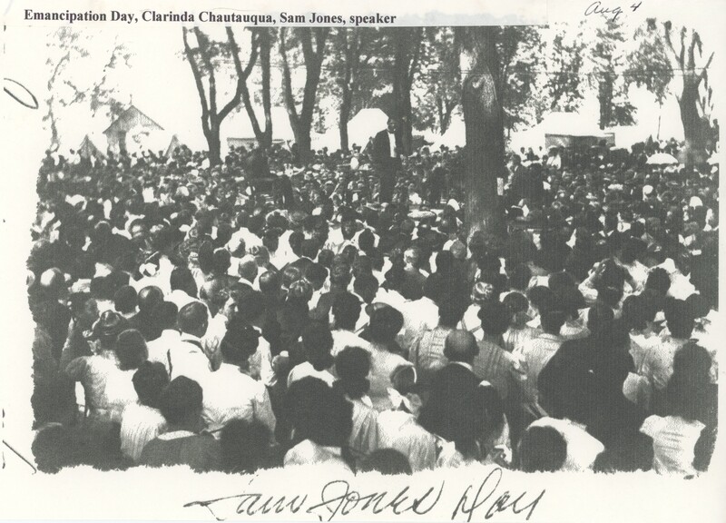 A large crowd surrounding and looking up at a person stood on a box giving a speech.