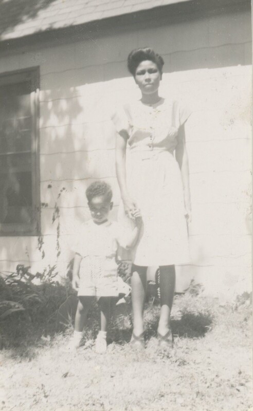 A person holding a little childs hand stood outside in the grass next to a house.