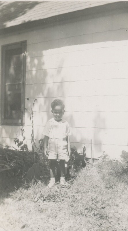 A little child stood in the grass in front of a house for a photo.