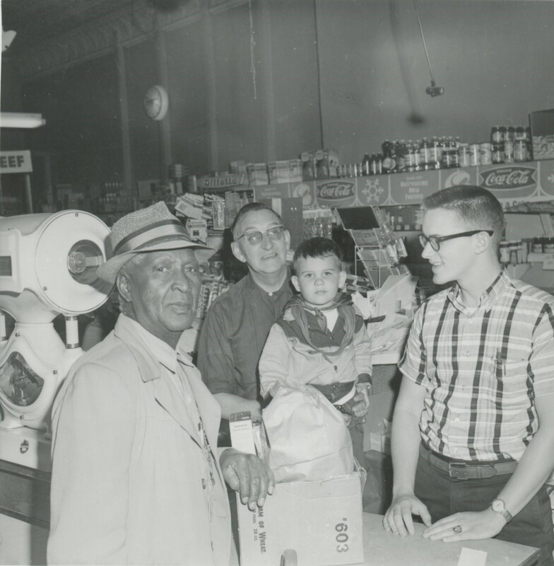 Three adults and a little child stood around a counter in a market.