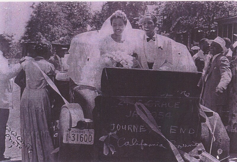A bride and groom sat in a wedding carrage after getting married with some wedding attendees surounding them sending them off.