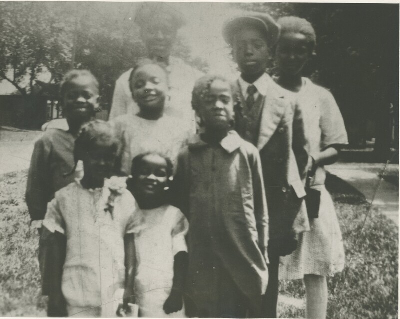 A group of eight children of varying ages clumped together for a photo outisde in the grass.