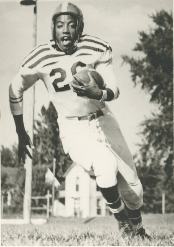 A young person in uniform running while holding a football playing a game.