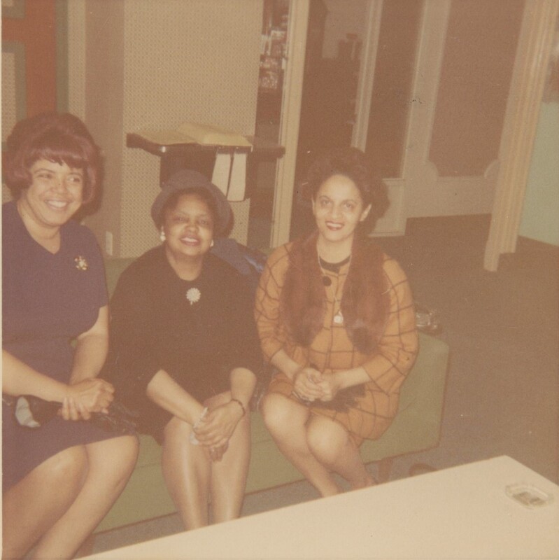 Three people sat next to eachother on a couch smiling for a photo in a room.