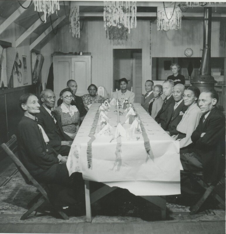 A group of people sat around a longer dining table set for a formal dinner.