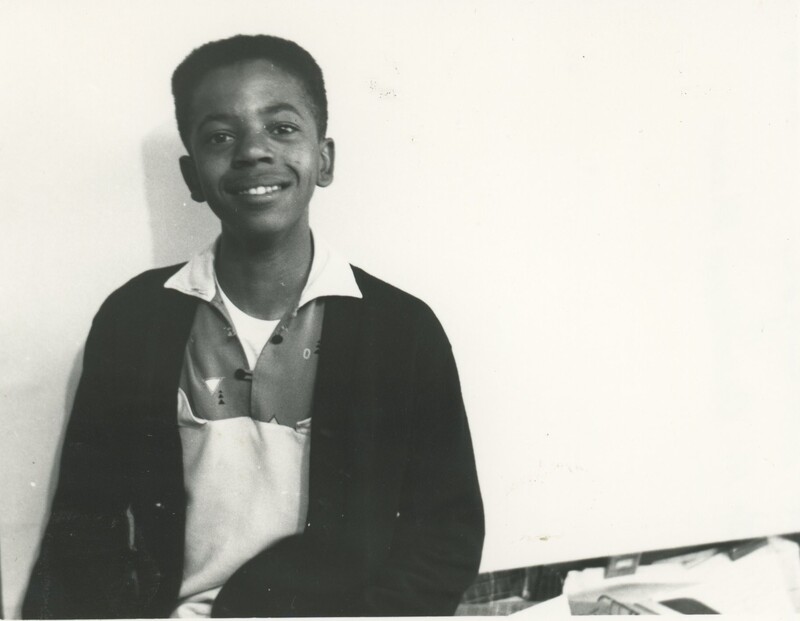 A young child sat and smiling for a photo off the the left of the frame from the waist up.