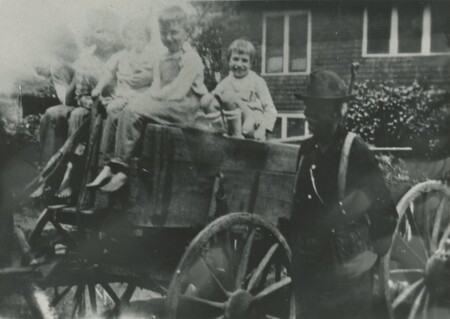 A person standing next to a horse drawn wagon with some children sat on top.