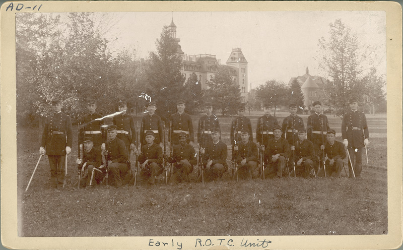 Photograph of the Department of Military Science and Tactics with George Washington Carver 4th from left in the front row kneeling. The Department of Military Science and Tactics was established in 1870 along with the S.A.T.C. as a result of a provision in the Morrill Land Grant Act. In 1916, Congress passed the National Defense Act, which provided for the establishment of the Reserve Officers Training Corps (R.O.T.C.). Old Main and Morrill Hall can be seen in the background.