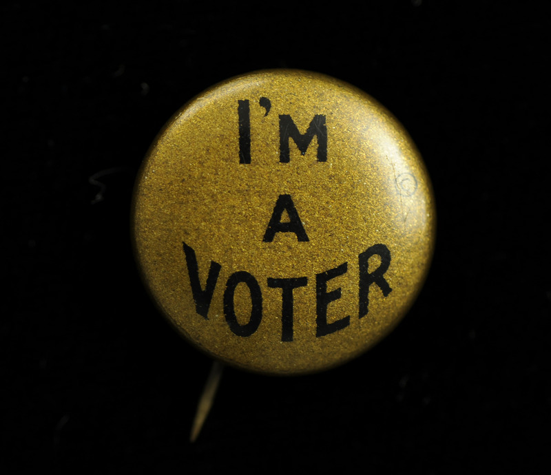 Round gold colored button with "I'M A VOTER" in black lettering on the front.