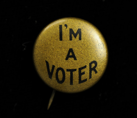 Round gold colored button with "I'M A VOTER" in black lettering on the front.