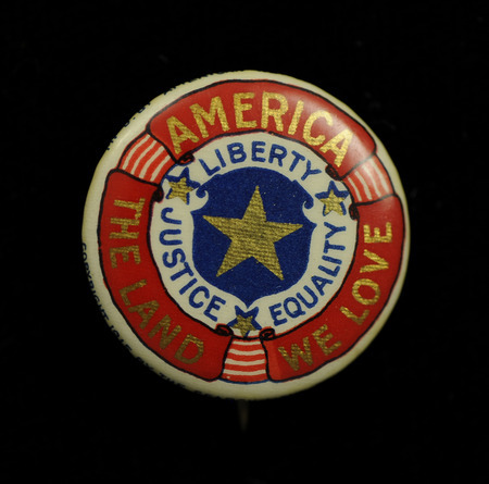Round, metal, white, 3 red scrolls around the outside circle of the button "America" "The Land" "We Love" inscribed in gold, the second circle of the button is white with blue letters "Liberty" gold star, "Justice" gold star, and "Equality" gold star. The inner and last circle of the button contains a blue circle with a gold star.