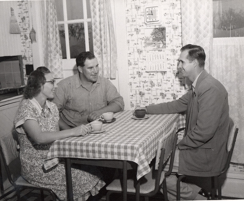 Photograph of a man and woman at a table having a discussion with a friend.