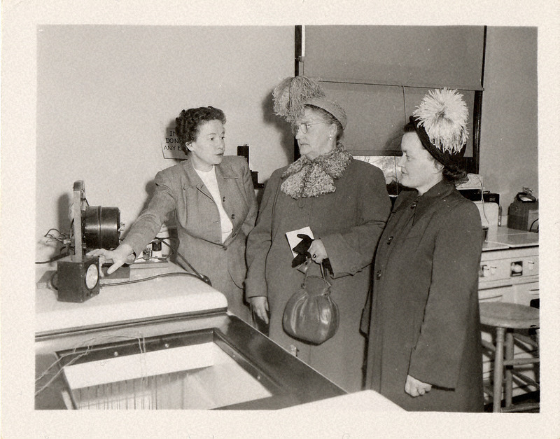 Photograph of three women standing in front of household equipment.