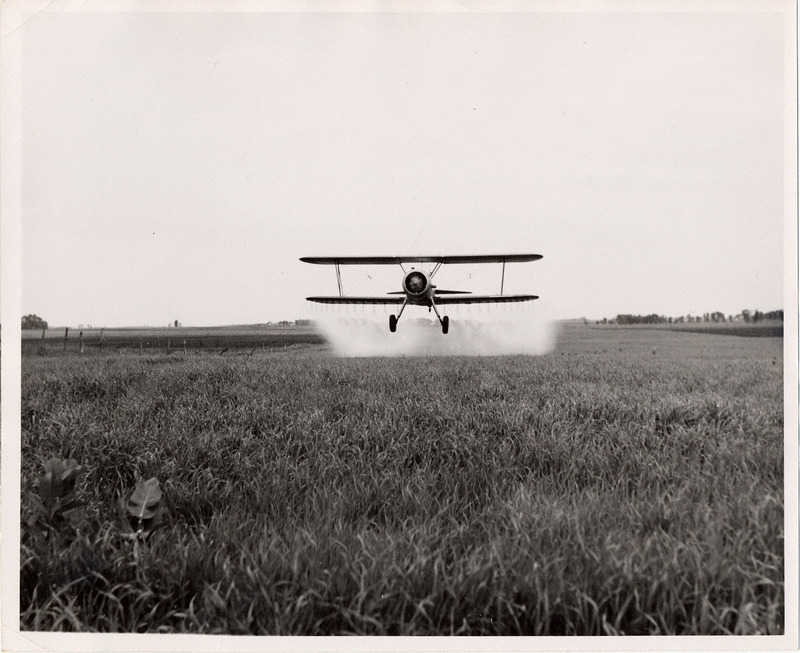 Photograph of a crop duster flying over a field.