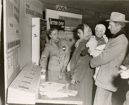 Photograph of a family of three and a woman standing in front of a Caravan Exhibit at the Iowa State Fair in 1957.
