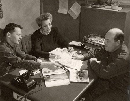 Photograph of Greta Bowers and a man discussing with another man in 1953 over Extension business.