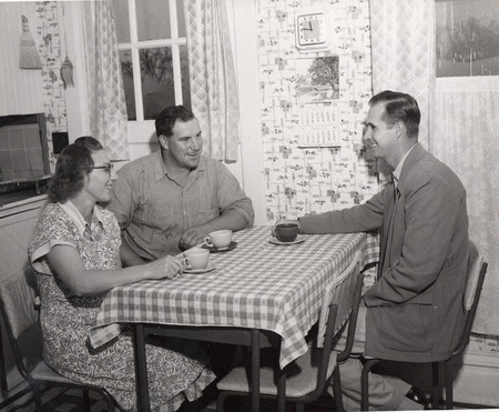 Photograph of a man and woman at a table having a discussion with a friend.