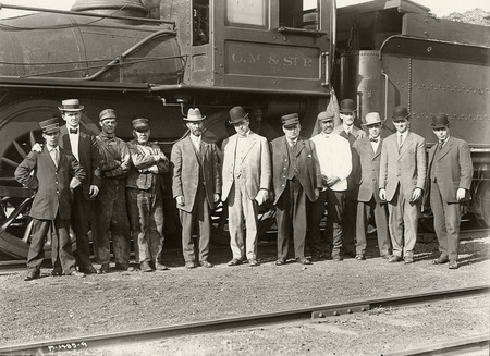 Photograph of a corn train's crew standing in front of the train. Perry Holden stands fifth from the left. Taken in 1910.