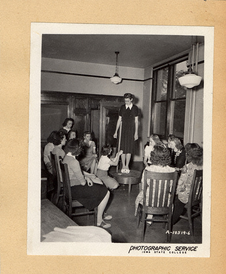 Photograph of a group of young women observing a dress being measured in 1942.