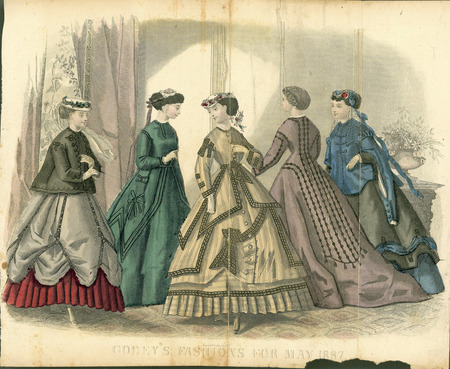 Five walking dresses all with long sleeves, jewel necklines, and full skirts. The young woman wears a loose jacket with long sleeves, a layered walking skirt where the top layer is pulled back with vertical belts to reveal the pleated underlayer, and a flower trimmed hat. The 2nd woman has a simpler dress with a belted waistline, bow trim on the floor length skirt, and a lace cap. The 3rd young woman wears a flower trimmed Eugenie hat; a striped dress with contrasting trim around the armscyes, waistline, cuffs, and skirt edges; and a complex walking skirt with multiple layers of differing shapes and sizes, center front buttons, a large bow, and a pleated hemline. The 4th woman has a simple dress with elaborate braid and tassel trim extending from the neckline and hips to the lower portion of the floor length skirt. The 5th woman has a loose jacket with complex sleeves over a dress with a layered, floor length skirt and a hat with lace and ribbon trim. (published for Godey's Fashions).