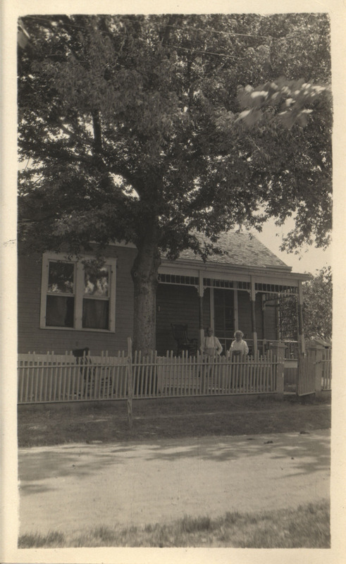 Photograph of Mr. and Mrs. Hayden standing on porch outside of their house with a large tree in foreground.