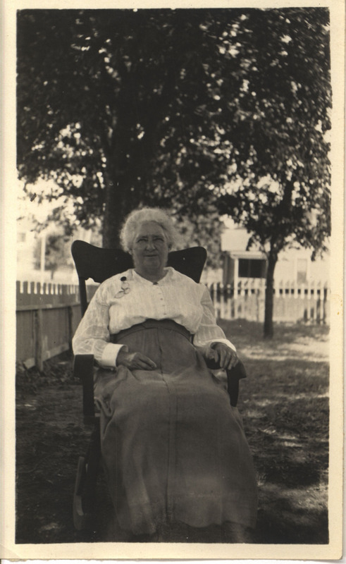 Photograph of Christina J. Hayden seated in a chair in front of a large tree.