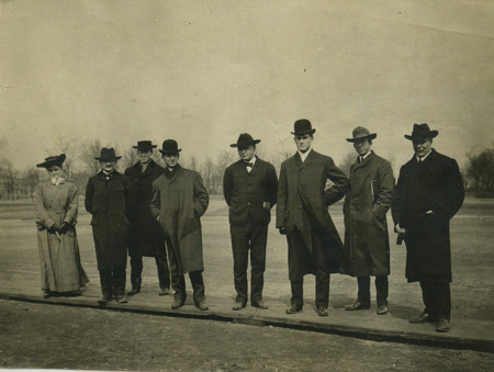 The woman is dressed in a coat, hat and gloves and most of the men are in overcoats and hats.