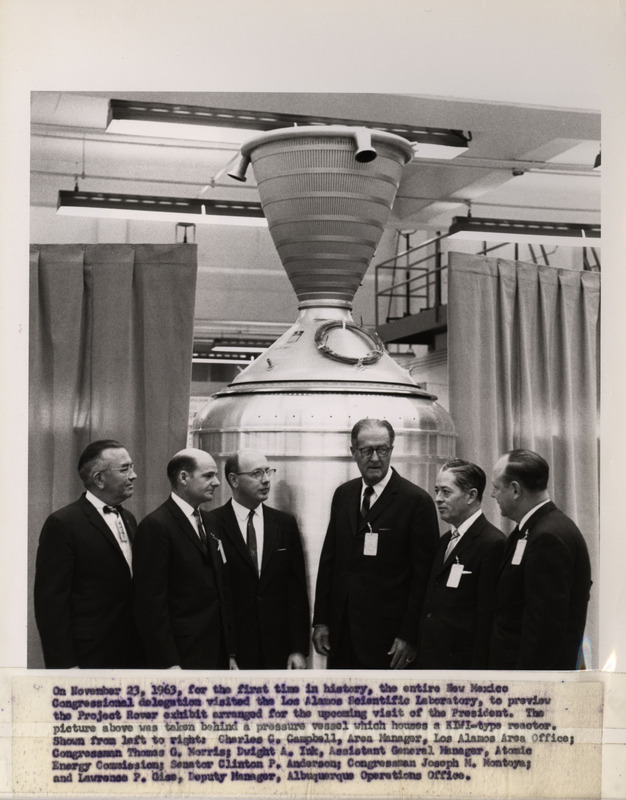 Annotation: "On November 23, 1963, for the first time in history, the entire New Mexico Congressional delegation visited the Los Alamos Scientific Laboratory, to preview the Project Rover exhibit arranged for the upcoming visit of the President. The picture above was taken behind a pressure vessel which houses a KIWI-type reactor. Shown from left to right: Charles C. Campbell, Area Manager, Los Alamos Area Office;Congressman Thomas G. Morris;Dwight A. Ink, Assistant General Manager, Atomic Energy Commission;Senator Clinton P. Anderson;Congressman Joseph M. Montoya;and Lawrence P. Gise, Deputy Manager, Albuquerque Operations office."