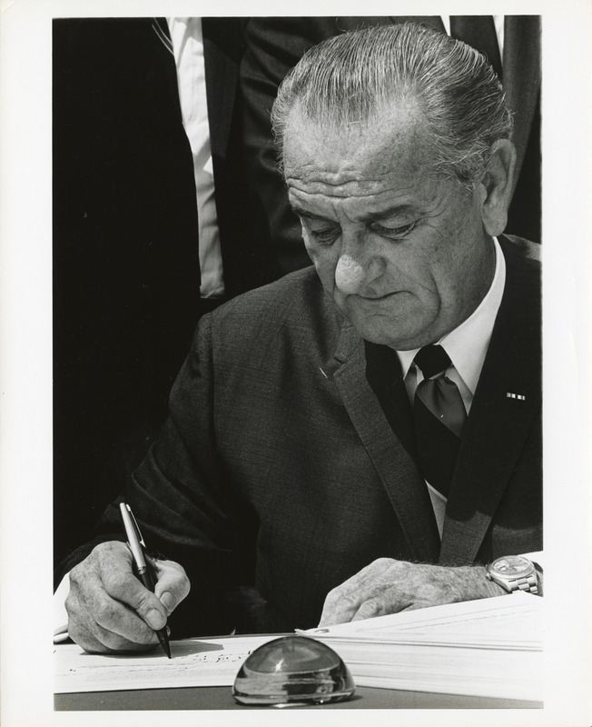 Photograph of Lyndon B. Johnson signing a document